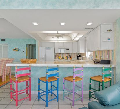Gather around your vibrant breakfast bar with colorful stools where morning coffee and conversations flow naturally in this cheerful coastal kitchen.