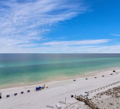 Pristine white sand beach stretches along emerald waters under brilliant blue skies dotted with wispy clouds.