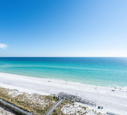 Pristine white sand beach stretches alongside crystal-clear turquoise waters under brilliant blue skies.