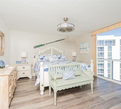 Your coastal bedroom features nautical charm with ocean-inspired bedding and expansive city views through floor-to-ceiling windows.