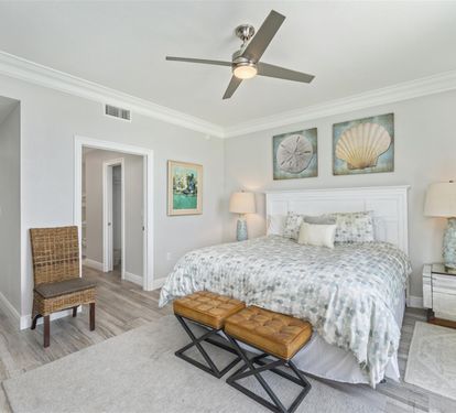 Relax in your coastal-inspired bedroom with ocean artwork, soft lighting, and a ceiling fan for comfort.