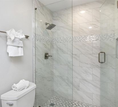Step into your luxurious marble-clad shower with rainfall head and mosaic accents. Fresh towels await nearby.