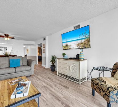 Relax in your bright living space with coastal-themed touches, modern furnishings, and a large TV displaying beautiful beach views.