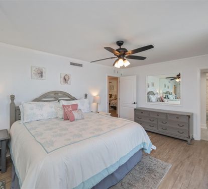 Unwind in your serene master bedroom, featuring soft coastal bedding and a gentle ceiling fan for perfect comfort.