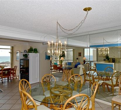 Your spacious oceanfront retreat features an open-plan living space where elegant chandeliers cast warm light over coastal-themed dining and lounging areas.