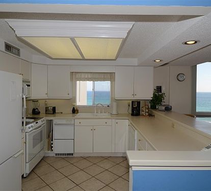 Cook with breathtaking ocean views streaming through your kitchen window, where white cabinets and warm lighting create the perfect coastal retreat.