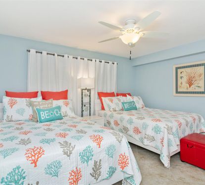 Drift off to sleep in this peaceful coastal-themed bedroom featuring twin beds with cheerful coral bedding and beach-inspired decor.
