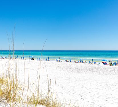 Pristine white sand stretches toward turquoise waters under clear blue skies. The beach offers powder-soft sand and gentle surf, perfect for a peaceful day by the sea.