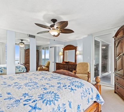 Sink into your elegant master bedroom with tropical ceiling fan, rich wood furnishings, and stunning ocean views through floor-to-ceiling windows.