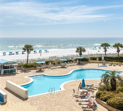 Oceanfront property overlooking a pristine beach and sparkling pool area with palm trees and sandy shores.