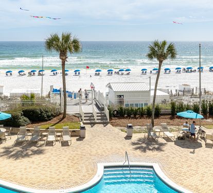 Beachfront pool area with direct beach access, colorful kites dancing overhead, and umbrellas dotting pristine white sand.