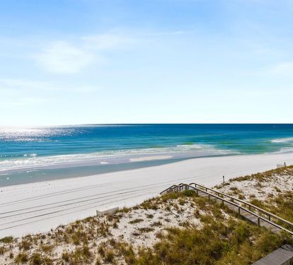 Pristine white sand beach stretches along turquoise waters, with wooden boardwalk leading through coastal dunes.
