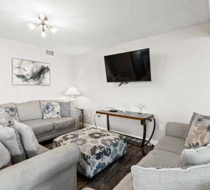 Relax in your spacious living room with plush gray seating, modern entertainment center, and elegant décor creating the perfect retreat.