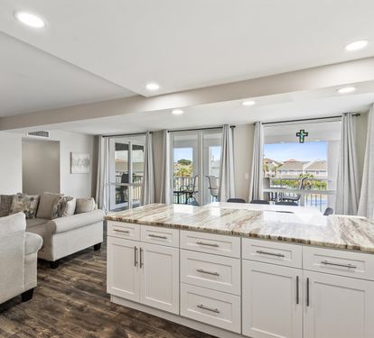 Your open-concept living flows seamlessly from marble kitchen island to plush seating, with stunning water views through floor-to-ceiling windows.