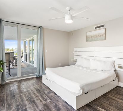 Relax in your modern bedroom with crisp white linens, private balcony access, and gentle ceiling fan keeping you cool.