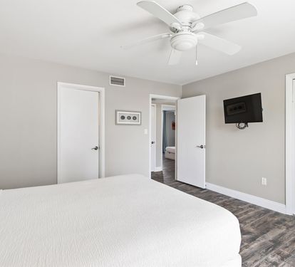 Relax in your bright, modern bedroom with comfortable bedding, ceiling fan, and wall-mounted TV for your entertainment.