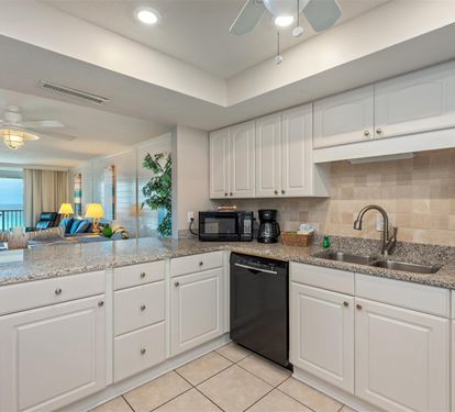 Prepare your favorite meals in this fully equipped kitchen featuring granite counters, white cabinetry, and modern appliances with stunning ocean views.