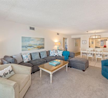 Your spacious living room flows seamlessly into the dining area, with coastal blues and comfortable seating perfect for gathering.