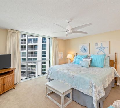 Relax in your serene coastal bedroom with aqua linens, warm lighting, and city views through floor-to-ceiling windows.