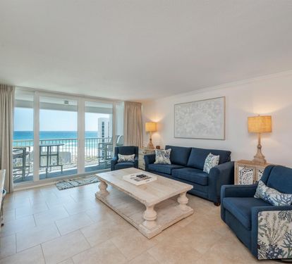 Relax in your spacious oceanfront living room with stunning sea views through floor-to-ceiling windows and comfortable coastal-themed seating.