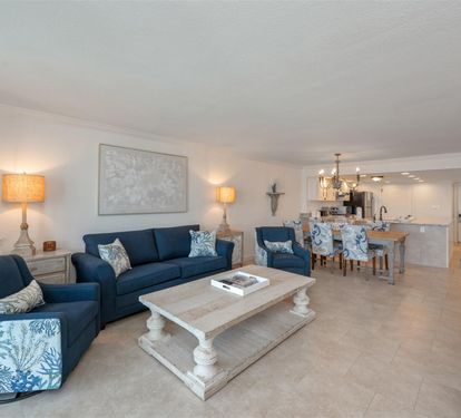 Relax in your elegant living room with plush navy seating, warm coastal lighting, and an open kitchen perfect for entertaining.