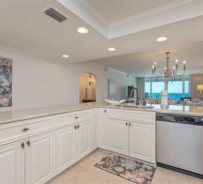 Your elegant white kitchen features granite countertops and stainless appliances, with stunning ocean views through the open living space.