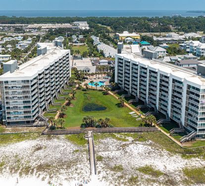 Aerial view of beachfront property buildings with pool area and direct boardwalk access to the sandy shore, situated in a coastal residential area.