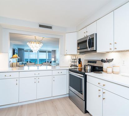 Your elegant kitchen opens to breathtaking ocean views, featuring modern appliances and pristine white cabinetry perfect for preparing memorable meals.