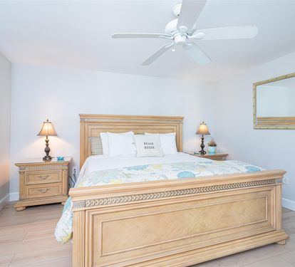 Sink into crisp linens and coastal comfort in your serene bedroom, where gentle ceiling fan breezes and warm bedside lighting create perfect relaxation.
