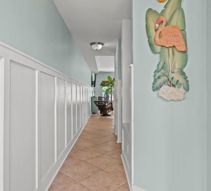 Step into your coastal retreat through this charming hallway adorned with tropical artwork and elegant wainscoting that sets the tone for relaxation.