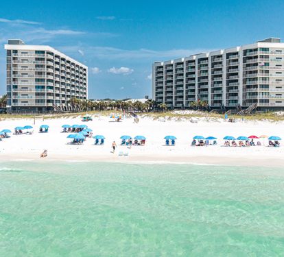 Beachfront property buildings with direct access to white sand beaches and crystal-clear turquoise waters, surrounded by palm trees and vacation atmosphere.