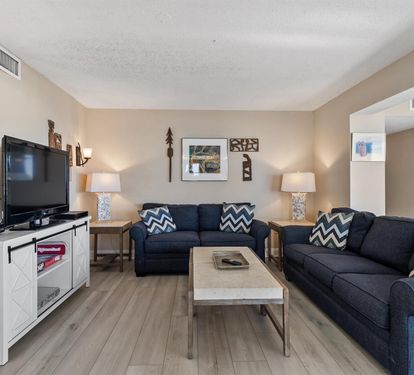 Unwind in your spacious living room with plush navy sofas, warm lighting, and entertainment center for cozy evenings together.