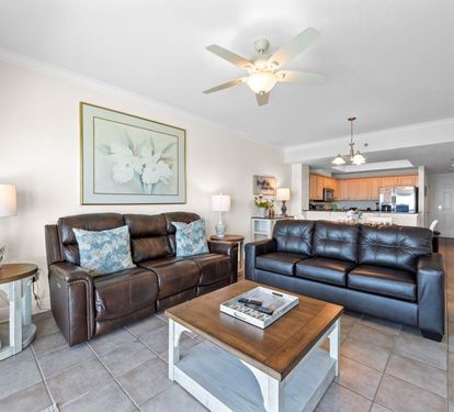 Relax in your spacious living room with comfortable leather seating, ceiling fan, and open concept design flowing into the full kitchen.