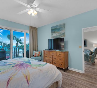 Primary king bedroom with Gulf views, balcony access, and a TV. Living-room furniture visible in the adjoining room has since been replaced.