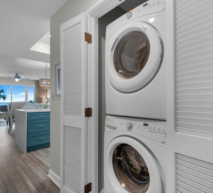 In-unit laundry with Gulf views beyond the living area. Living-room furniture shown has since been replaced.