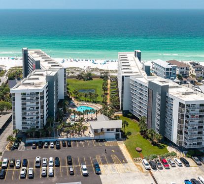 A beachfront resort property featuring modern buildings, pools, and green spaces overlooking pristine white sand and turquoise waters.